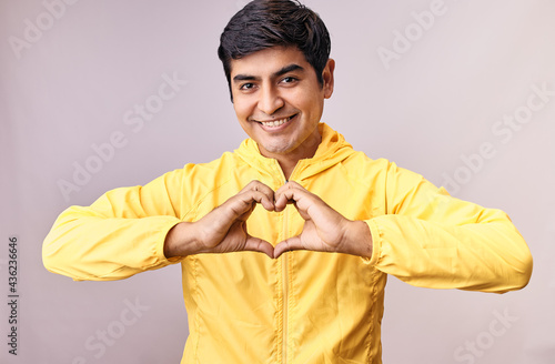 Hombre joven y feliz hace gestos de amor con sus manos. Modelo aislado en fondo blanco con casaca amarilla photo