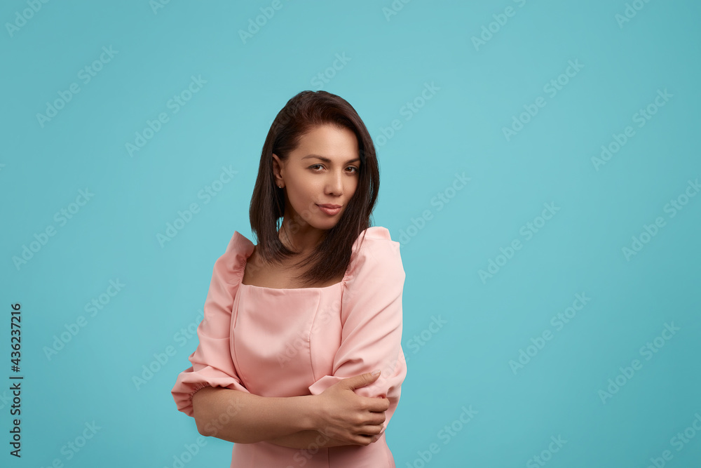 Playful coquettish caucasian female in pink dress, smiling shyly at camera as if flirting. Having joyful expression on her face, isolated over blue background. People expression concept. Playful coquettish caucasian female in pink dress, smiling shyly at camera as if flirting. Having joyful expression on her face, isolated over blue background. People expression concept.