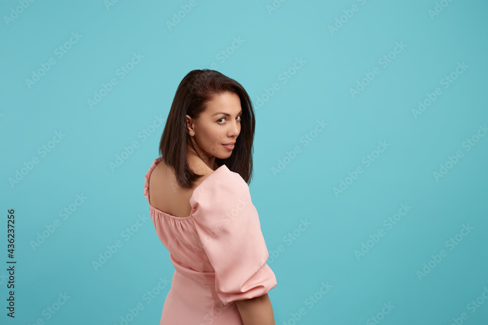 Love adventure. Hey you, come with me. Pleasant looking woman in pink dress looking from back like flirting, sexually smile. Isolated over blue background. People expression concept. Love adventure. Hey you, come with me. Pleasant looking woman in pink dress looking from back like flirting, sexually smile. Isolated over blue background. People expression concept.