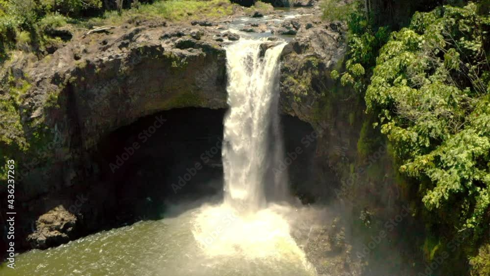 Aerial Tilt Down Shot Of Waterfall Amidst Rock Formation By Plants On Sunny Day - Big Island, Hi Aerial Tilt Down Shot Of Waterfall Amidst Rock Formation By Plants On Sunny Day - Big Island, Hi