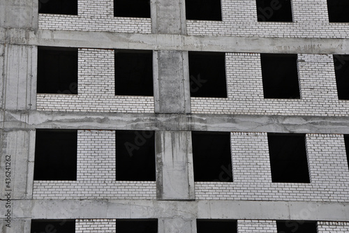 Facade part of constructed building with gray concrete framework, white brickwork and black window holes.