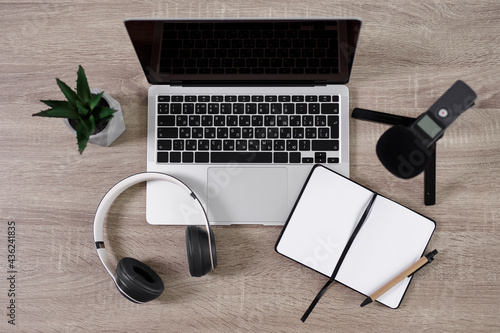 podcast and blogging concept - top view of workplace with laptop, microphone, headphones, open notepad and pen over wooden table background photo