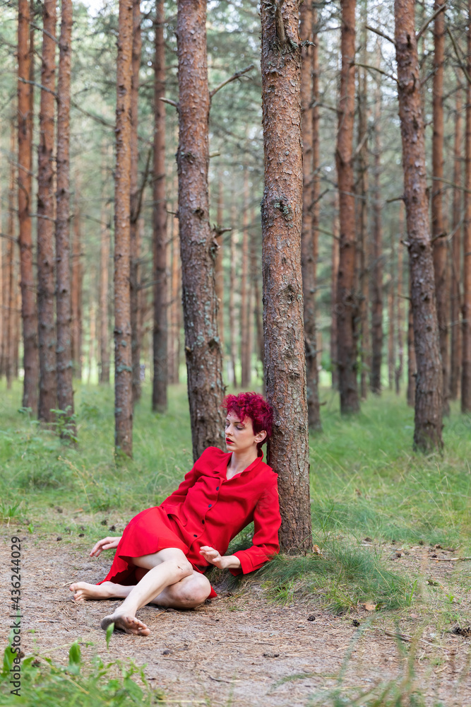Young woman in red dress posing in pine forest Young woman in red dress posing in pine forest