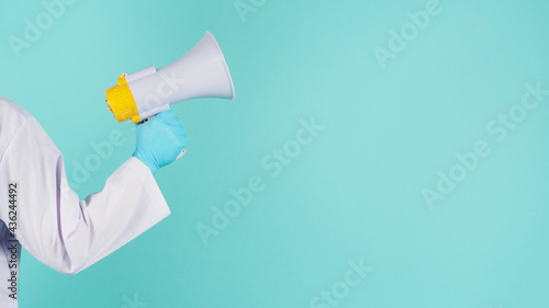 Megaphone in hand.Man wear doctor gown and blue medical glove on mint green or Tiffany Blue background. Studio shooting.