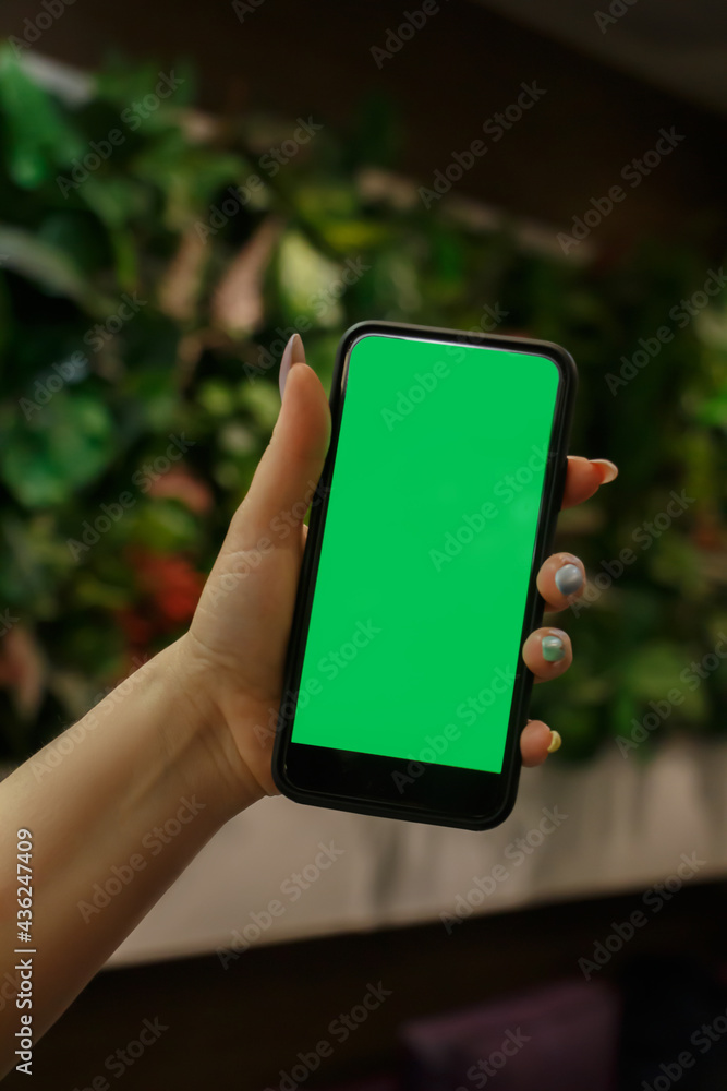 The human hand shows a mobile smartphone with a green screen in an upright position .Mock up mobile. blurred background