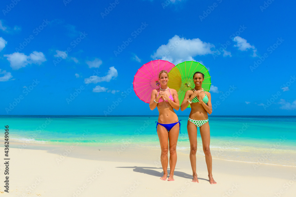Girls having fun at the beach, standing on the seashore with pink and green umbrellas, interracial, black 