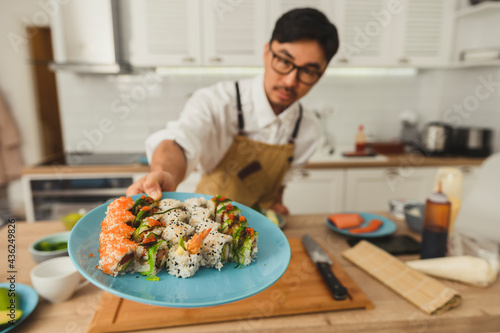 Asian chef hold plate with set of sushi rolls served on a kitchen background. Selective focus on a plate