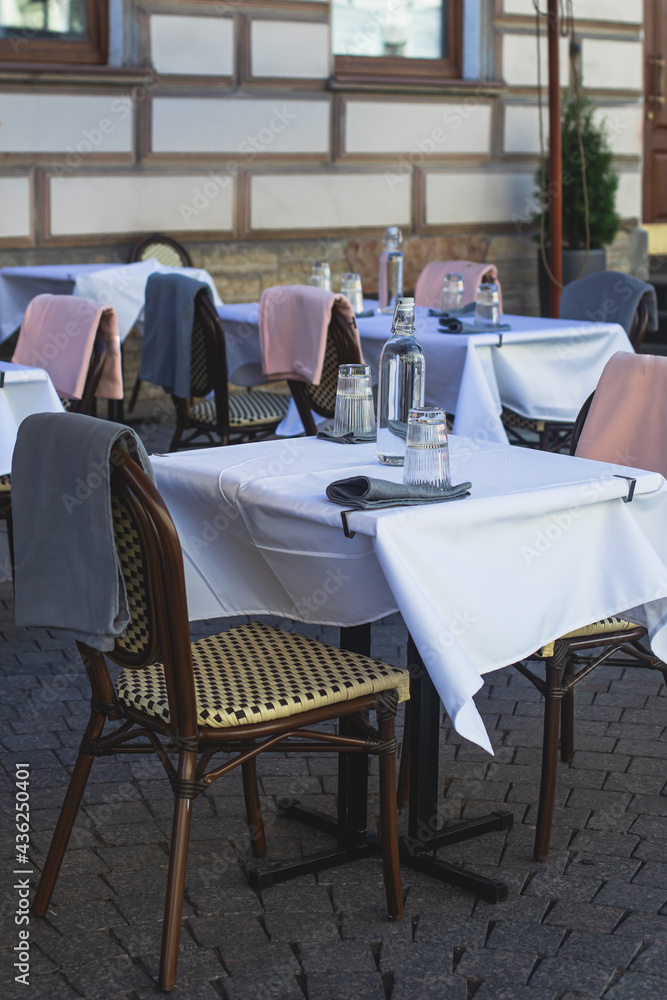 View of empty street cafe restaurant outdoor terrace veranda decoration on pedestrian european street, with chairs, tables decorated with white tablecoth, pink and grey blanket, bottles of water
