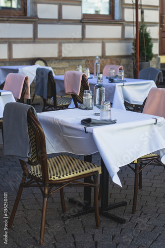 View of empty street cafe restaurant outdoor terrace veranda decoration on pedestrian european street, with chairs, tables decorated with white tablecoth, pink and grey blanket, bottles of water © tsuguliev