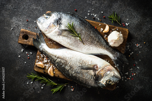 Fototapeta Naklejka Na Ścianę i Meble -  Fresh fish dorado on black stone table with ingredients for cooking. Top view.