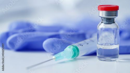 Close-up glass ampoule with vaccine against coronavirus,COVID19,influenza,diabete and other diseases andsyringe on table against background of medical gloves,selective focus.Vaccination banner concept