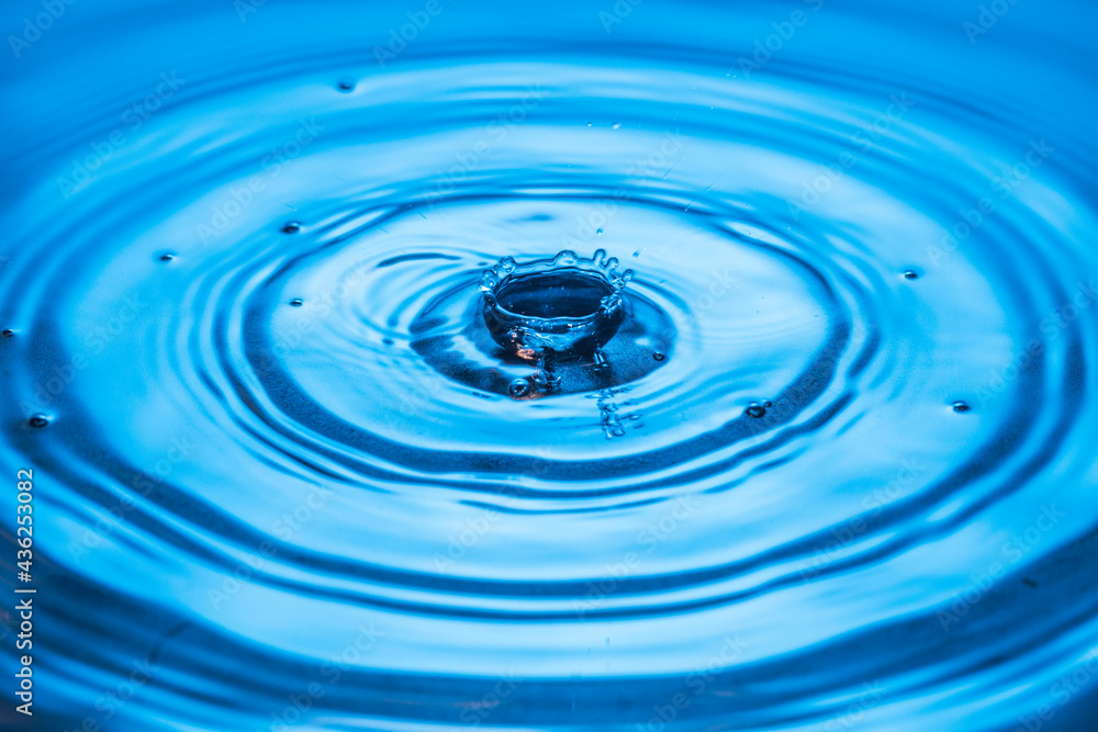 Macro view of drops making circles on blue water surface isolated on background.