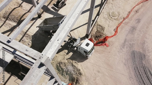 Beams With Steel Reinforcement. Dump Truck Unloads Sand in Construction. Aerial view. Unloading soil. Reinforced Concrete Frame Of An Industrial Building. Camera Flight On A Construction Site.