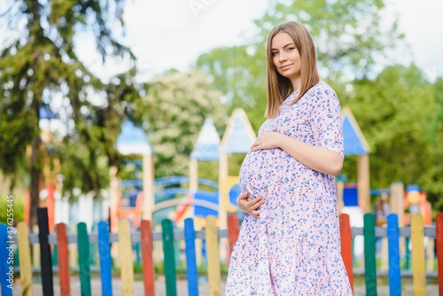 pregnant woman stands in the park near the playground where children play.