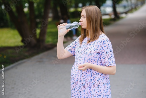 Pregnant woman stands in the park with a bottle of water. copy space