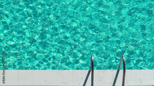 Beautiful light ripples on the water surface in the pool. Sun glare on turquoise water. Hot sunny day by the swimming pool. Summer chill. Holidays. Vacation. Handrails. Relax and calmness. photo