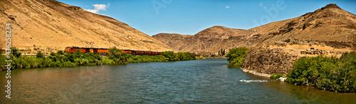 Yakima River Canyon scenic drive in a horizontal panorama showing the river, the canyon walls and the blue sky.