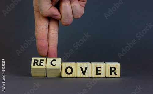 Time to recover symbol. Businessman turns wooden cubes and changes the word 'over' to 'recover'. Beautiful grey table, grey background. Business, over or recover concept. Copy space.