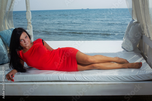 Fotografie Young woman in short red dress  lying and behind Mediterranean Sea