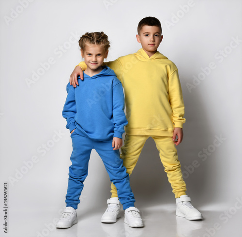 Studio portrait of a cool little boy and girl dressed in stylish bright sports suits with sweatshirts and pants on a white background. Children\'s sports style concept. Banner.