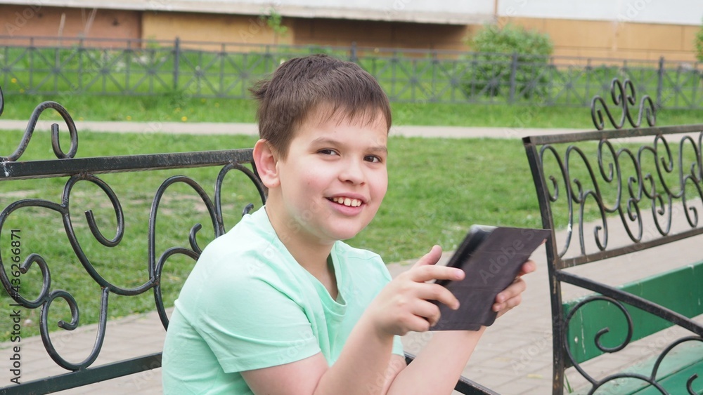 Teenage Boy On Park Bench Using Laptop And Digital Tablet chatting with friends, watching movies or cartoons, playing a video game Teenage Boy On Park Bench Using Laptop And Digital Tablet chatting with friends, watching movies or cartoons, playing a video game