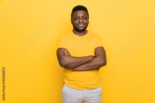 Portrait of young attractive candid afro american male looking at camera, hands crossed, wearing modern yellow outfit isolated over bright color yellow background