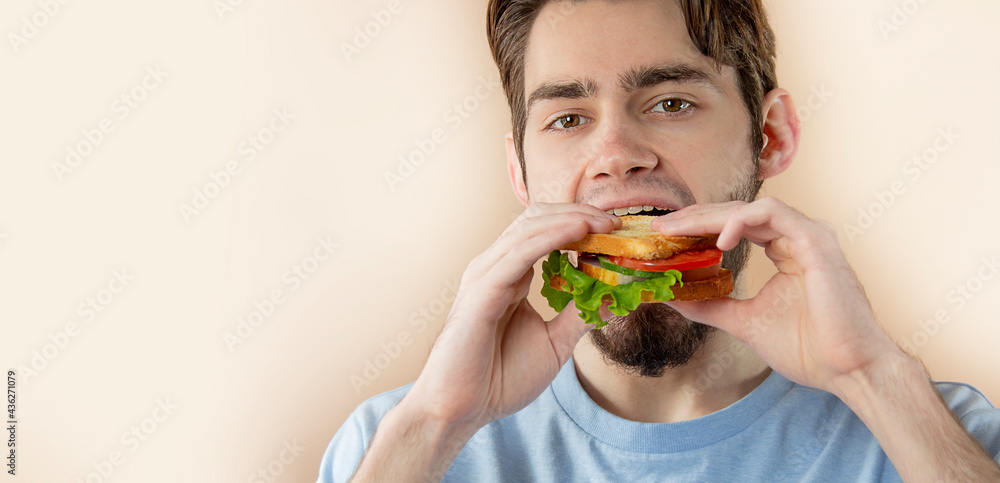 Hamburger. The man opened his mouth to eat a hamburger. The guy is eating a hamburger. Portrait of a man with a hamburger in his hands. Banner. Copy space Hamburger. The man opened his mouth to eat a hamburger. The guy is eating a hamburger. Portrait of a man with a hamburger in his hands. Banner. Copy space