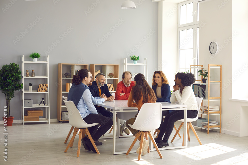 Team of mixed race business people sitting around big table in modern office space. Group of diverse company employees discussing projects and taking decisions together in corporate meeting