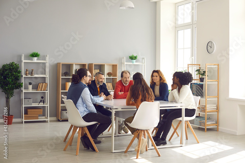Team of mixed race business people sitting around big table in modern office space. Group of diverse company employees discussing projects and taking decisions together in corporate meeting