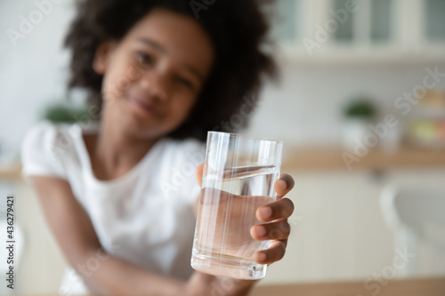 Crop close up of happy small African American girl child hold glass enjoy clean clear mineral water. Smiling little biracial kid feel thirsty recommend aqua for body hydration. Healthy life concept.