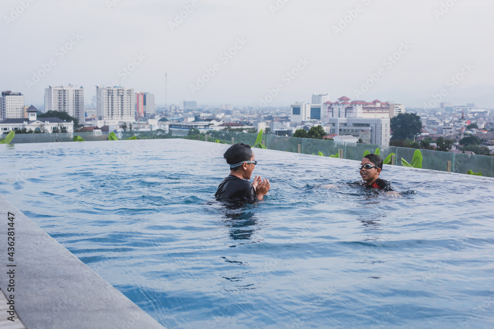 Happy two brothers wearing glasses having fun on infinity pool with city view background