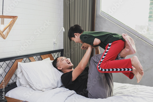 Asian young father playing with his little boy and having fun together on the bed