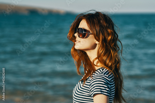 red-haired woman in sunglasses on the beach near the blue sea and mountains in the background