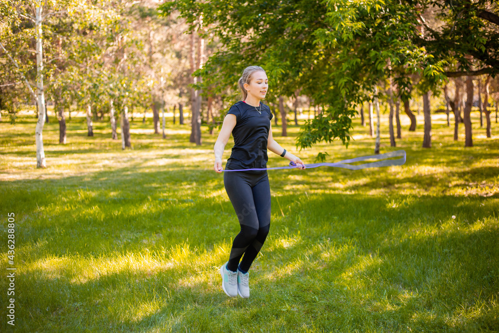 Young woman jumping rope on the lawn in a summer park. Jumping model. The concept of a healthy lifestyle and outdoor sports. Young woman jumping rope on the lawn in a summer park. Jumping model. The concept of a healthy lifestyle and outdoor sports.