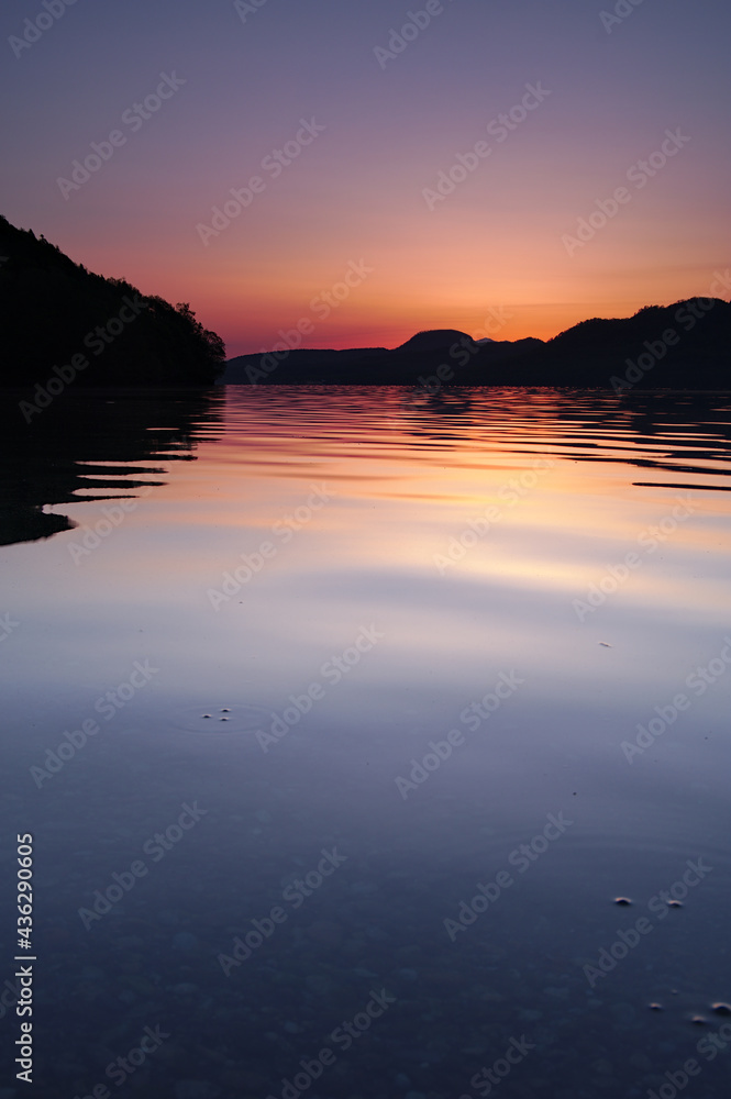 薄いオレンジ色の夜明けに穏やかな湖面の湖。