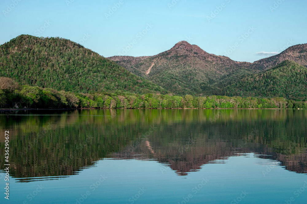 静水の湖面に映る湖畔の森と山々と空。