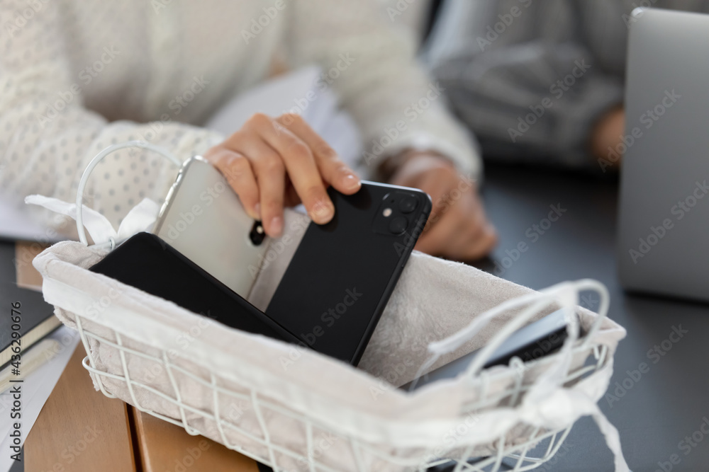 Close up cropped of young woman employee businesswoman putting phone in  basket, involed in meeting with colleague, free from smartphone, no  cellphone zone in office or digital detox concept Stock Photo