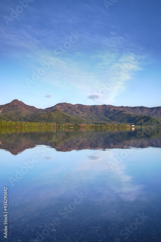 静水の湖面に映る湖畔の森と山々と空。 © Masa Tsuchiya