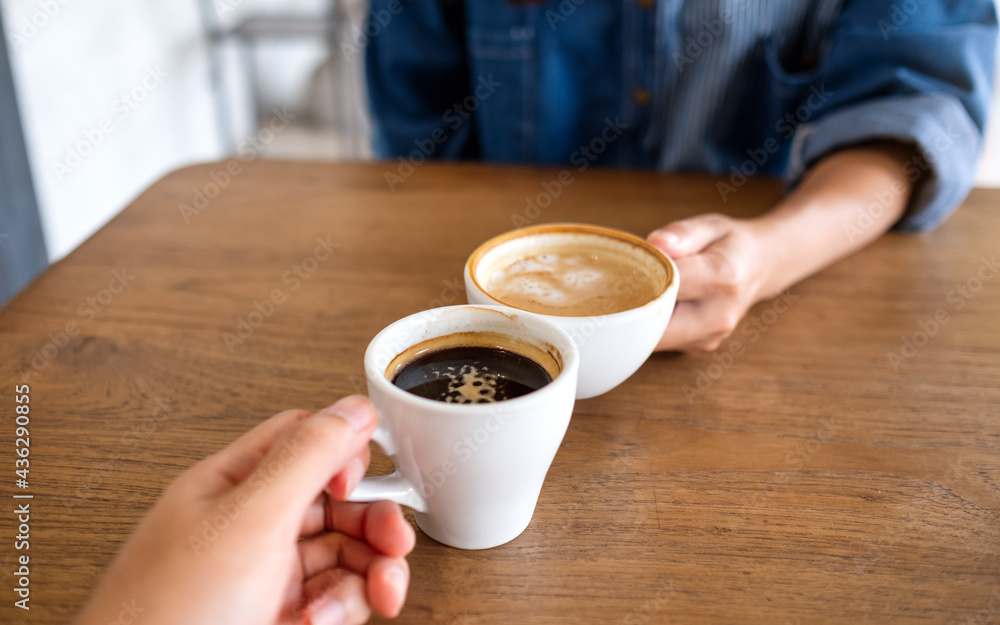 Closeup image of a woman and a man clinking coffee cups together in cafe