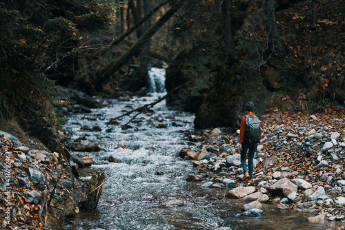 woman in the mountains near the river with a backpack on her back and a forest in the background