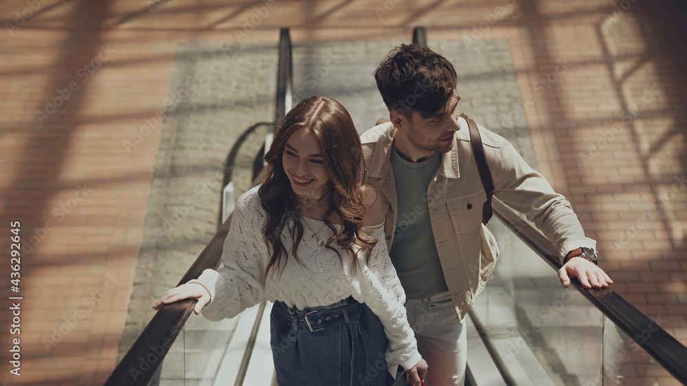 Naklejka premium high angle view of happy man and woman on escalator in shopping mall.