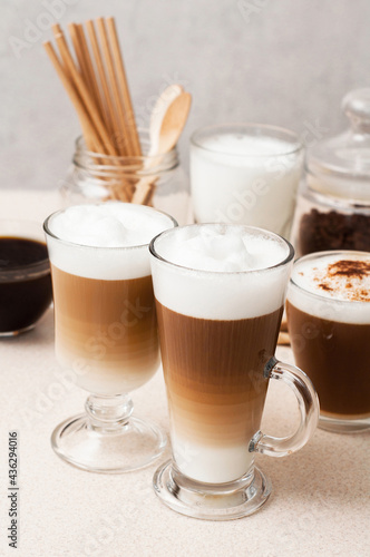 Coffee Latte macchiato with foam on a background of cups with coffee drinks and milk in glass cup on a table