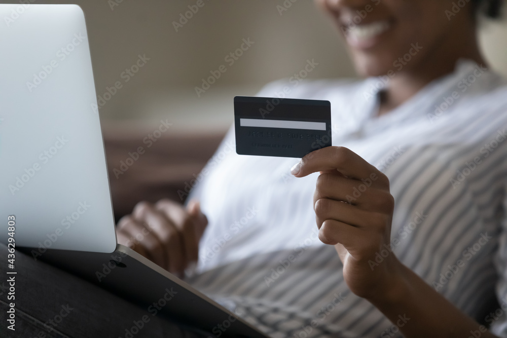 Close up focus on plastic credit card in female biracial hands, happy young african american female client paying for goods or services online using computer application, shopping in internet store. Close up focus on plastic credit card in female biracial hands, happy young african american female client paying for goods or services online using computer application, shopping in internet store.