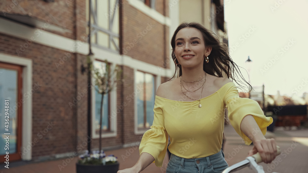 joyful young woman in yellow blouse smiling while riding on bicycle outside.