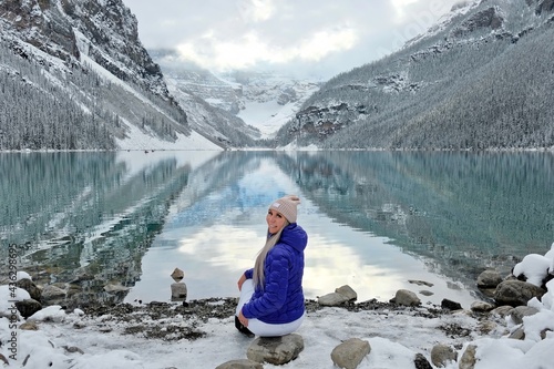 Attractive smiling woman in sport clothes on lake shore by snowy mountains. Early winter on Lake Louise in Banff National Park. Alberta. Canada