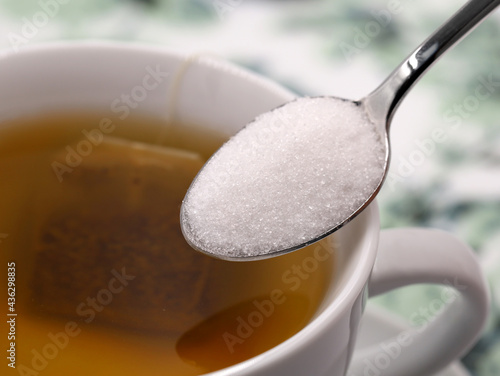 Billede på lærred close up of silver spoon with white sugar over tea cup