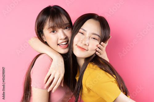 Portrait of two beautiful young Asian girls posing on pink background