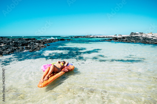Beautiful beach and tropical ocean water with pretty woman lay down on a colorful inflatable mattress lilo relaxing and enjoying the sea nature and the beach in summer holiday vacation