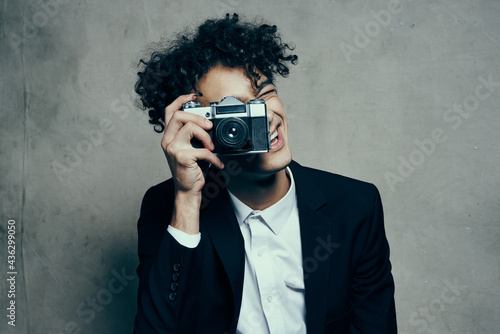 curly-haired man in a classic suit looks at the camera in his hand studio hobby