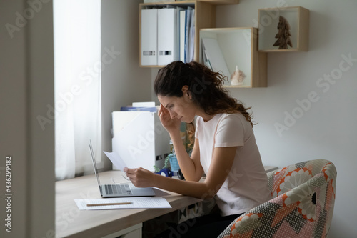Stressed unhappy woman reading paper correspondence at home office, feeling confused of getting bad news, bank mortgage loan rejection, eviction letter or dismissal notice, having financial problems.